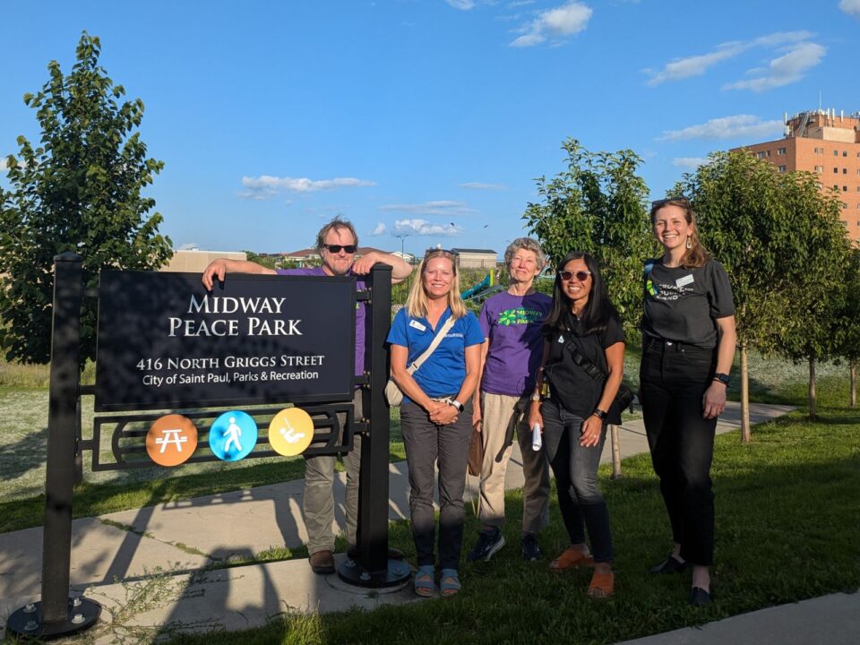 Five adults standing beside a park sign that reads 