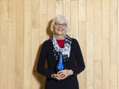 Barb Thoman holding a blue-swirled glass raindrop award. 