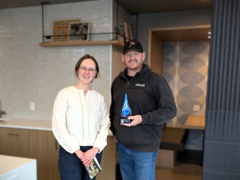 Two smiling people stand, the person on the right is holding a blue-swirled glass raindrop award.