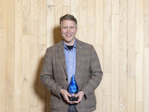 Ben Johnson holding a blue-swirled glass raindrop award.