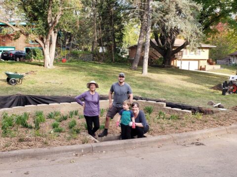 Three adults and a child stand in a newly planted residential rain garden along a street curb. 